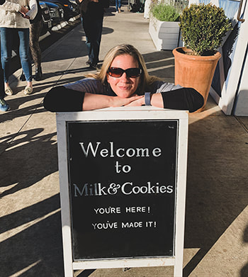 Woman posing in front of a black and white sign for Tiny's Milk & Cookies